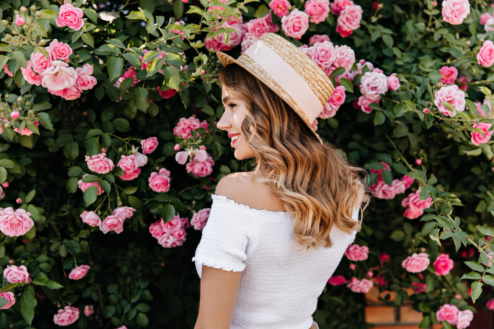 lovely-blonde-girl-summer-hat-looking-flowers-with-smile-pleased-curly-woman-relaxing-during-photoshoot-with-roses