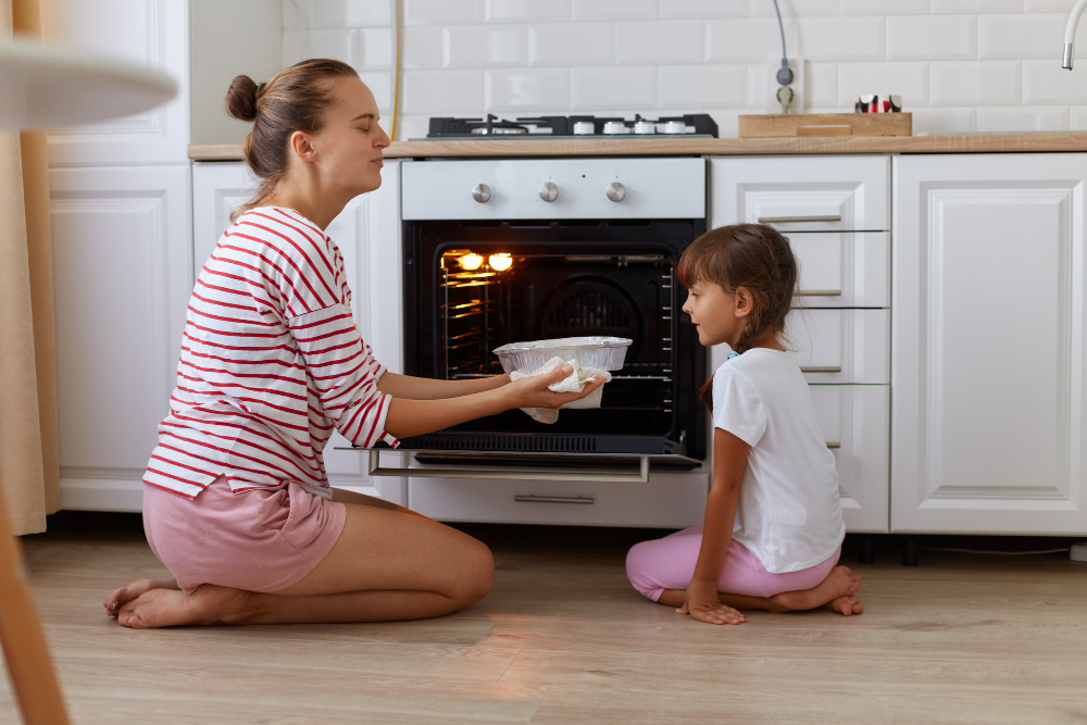 Portrait Happy Young Woman Taking Baking Out Oven Her Daughter Looking Tasty Sweets People Wearing Casual Clothing Sitting Floor Kitchen Cooking Together