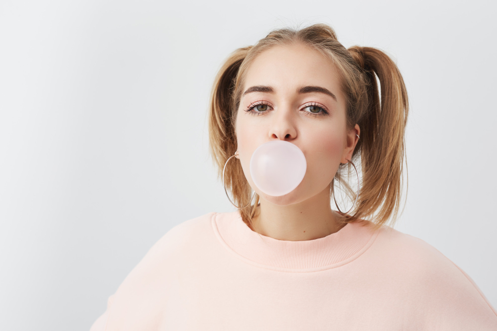beautiful-pretty-funny-young-girl-blowing-bubble-from-chewing-gum-blonde-female-with-two-ponytails-head-wearing-pink-sweatshirt-posing