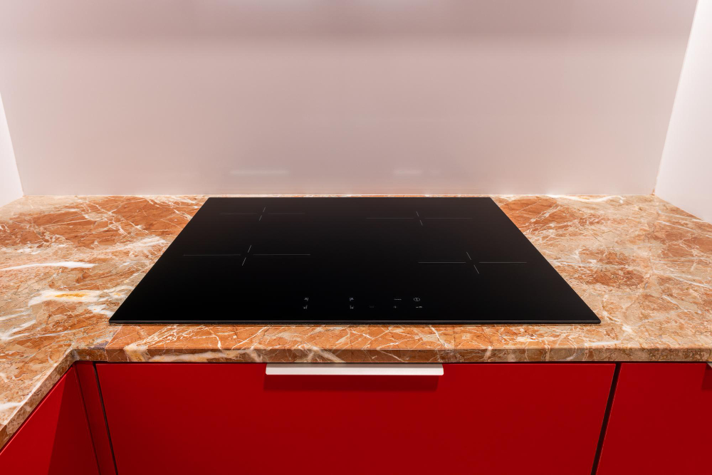 black-induction-hob-with-four-burners-is-built-into-beige-marble-countertop-red-kitchen-cabinet