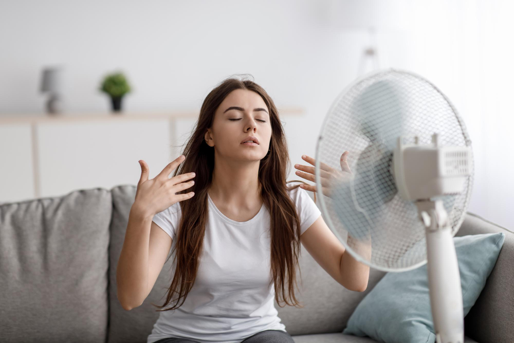 Sad Young European Woman Suffering From Heat Sits Sofa Catches Cold Air From Fan Waves Hands