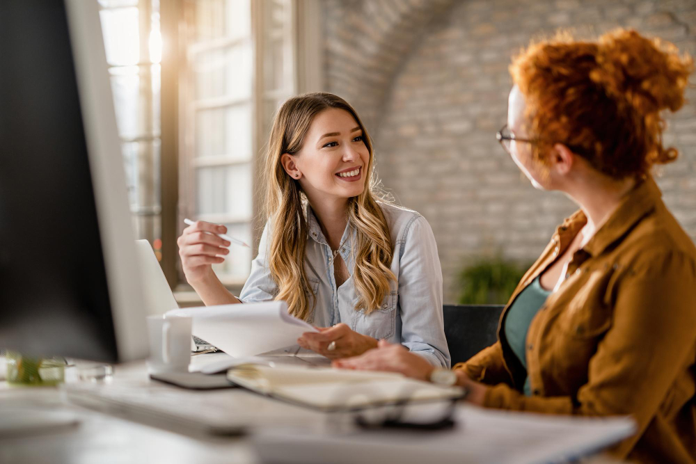 Smiling Creative Businesswoman Going Through Paperwork Talking Her Female Colleague Office